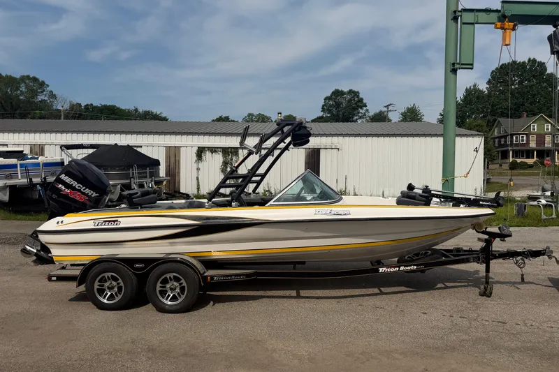 Slide: The Image of 2013 Triton 220 Escape boat on trailer, parked outdoors near a storage facility. - 0