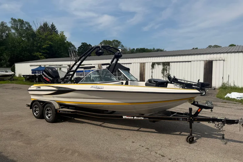 Slide: The Image of 2013 Triton 220 Escape boat on trailer, parked outdoors near storage buildings. - 6