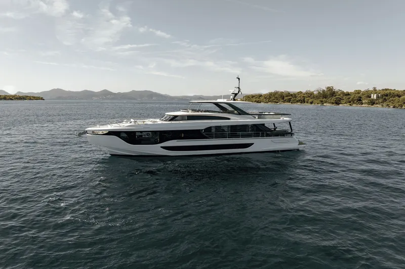 Slide: The Image of The 2027 Azimut Grande 26M cruises on calm waters with a wooded shoreline in the background. - 2