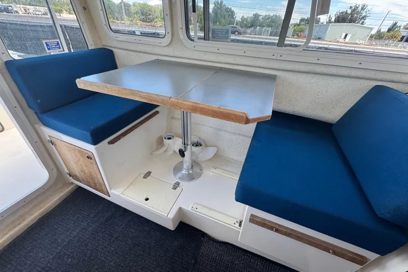 Slide: The Image of Interior of a 2013 C-Dory 22' Cruiser with blue cushioned seating and a table. - 46