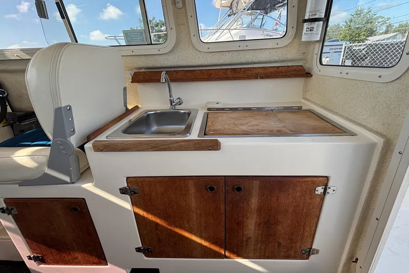 Slide: The Image of The interior view shows a compact galley with a sink and wooden countertop in a C-Dory 22' Cruiser. - 11