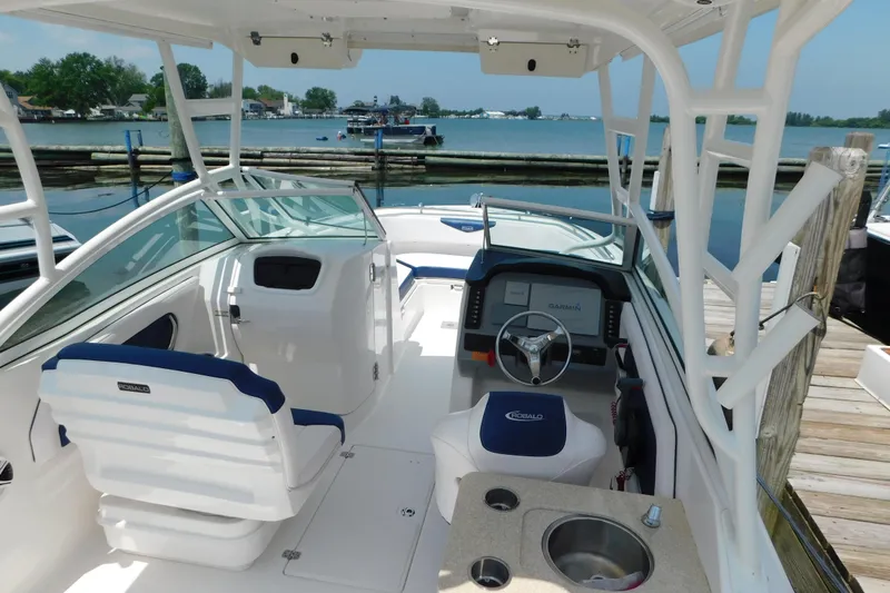 Slide: The Image of 2018 Robalo R247 Dual Console boat interior with helm, seating, and sink, docked by the water. - 14