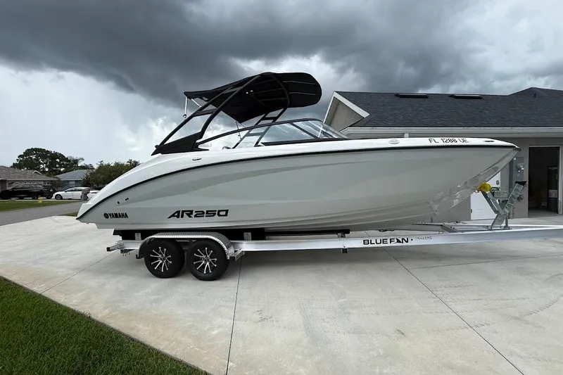 Slide: The Image of 2025 Yamaha Boats AR250 on trailer, parked in driveway under cloudy sky. - 5