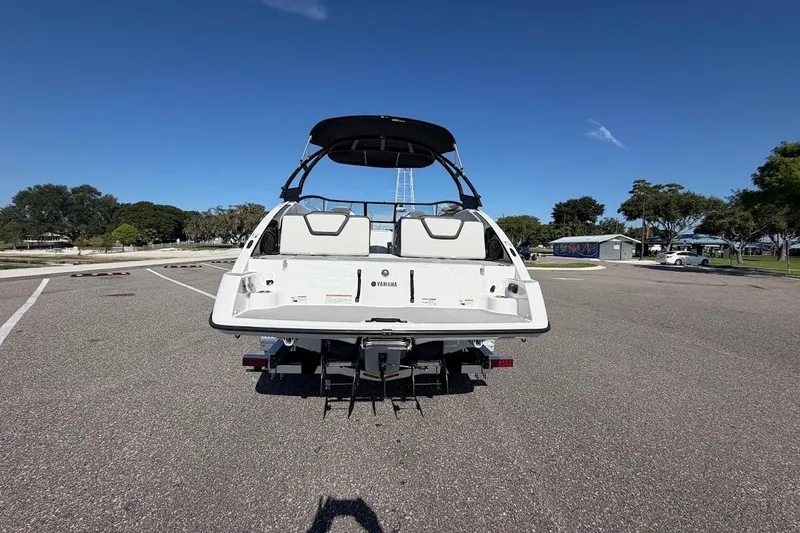 Slide: The Image of 2025 Yamaha Boats AR250, rear view, parked on asphalt under clear blue sky. - 33