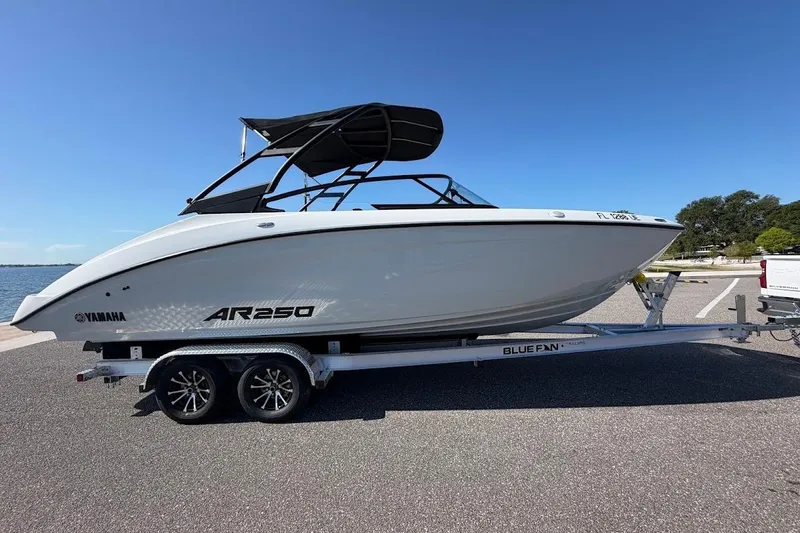 The Image of 2025 Yamaha Boats AR250 on trailer, sleek design, parked near waterfront under clear blue sky. - 0