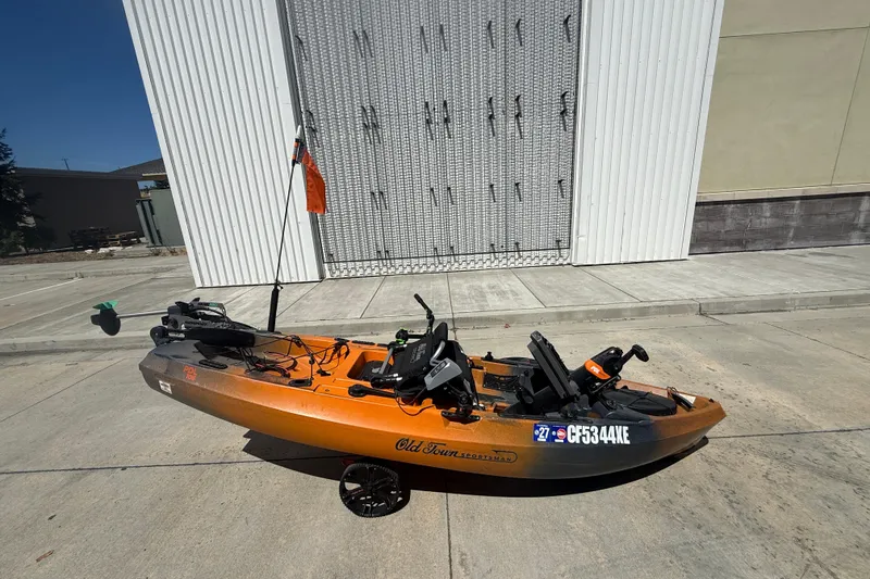 The Image of Orange OldTown Sportsman PDL 106 kayak, 2023 model, parked on concrete near a building. - 0