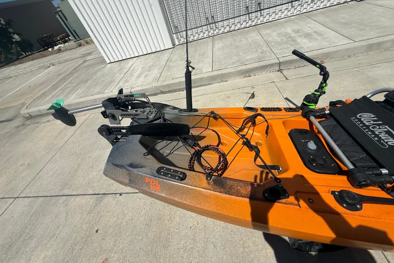 Slide: The Image of Orange OldTown Sportsman PDL 106 kayak with mounted motor, parked on concrete. - 3