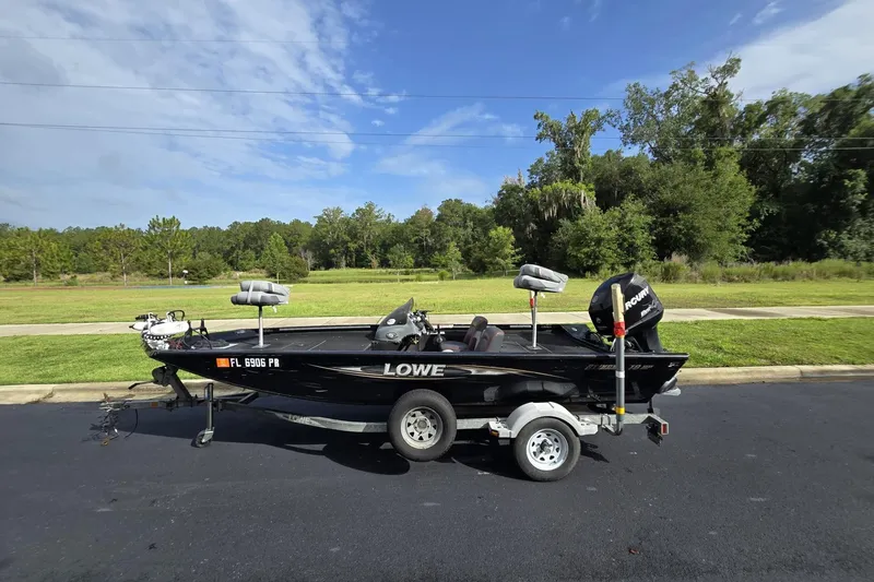 The Image of 2014 Lowe Stinger 18 HP boat on trailer, parked on a road with grassy background. - 0