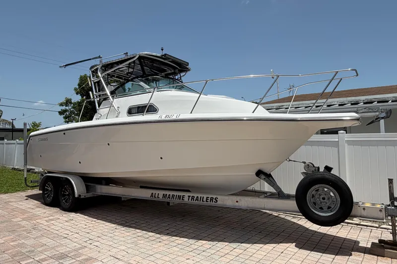 The Image of 2001 Stamas 270 Express boat on trailer, parked on a paved driveway under clear blue sky. - 1