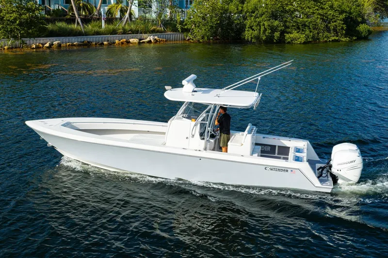 Slide: The Image of 2022 Contender 32 ST boat cruising on a calm waterway, surrounded by lush greenery. - 15