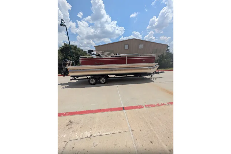 The Image of 2026 Sun Tracker Sportfish 24 XP3 pontoon boat on trailer, parked outdoors under a blue sky. - 0