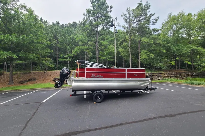 The Image of 2026 Sun Tracker Party Barge 18 DLX pontoon boat parked in a wooded area. - 0