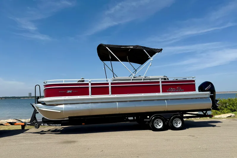 Slide: The Image of 2026 Sun Tracker Sportfish 24 XP3 pontoon boat on trailer by a lake. - 12
