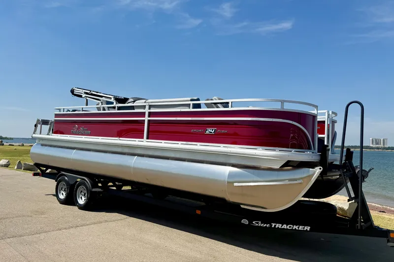 The Image of 2026 Sun Tracker Sportfish 24 XP3 pontoon boat on trailer by a lake. - 0