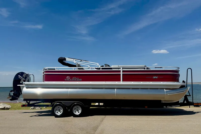 Slide: The Image of 2026 Sun Tracker Sportfish 24 XP3 pontoon boat on trailer by a lake. - 2