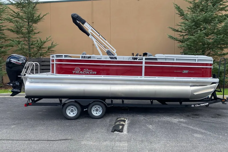The Image of 2026 Sun Tracker SportFish 22 DLX pontoon boat on trailer, parked outdoors. - 0