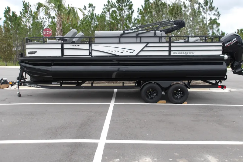 The Image of 2026 Ranger 220F pontoon boat on trailer in parking lot, surrounded by trees. - 1
