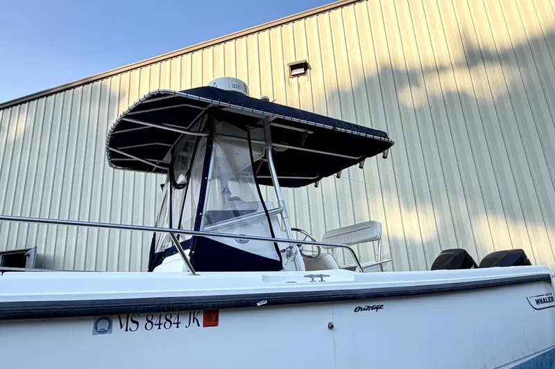 Slide: The Image of 2000 Boston Whaler 260 Outrage boat with canopy, docked near a metal building. - 5