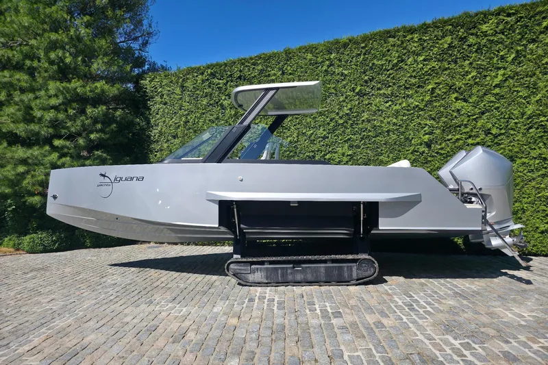 The Image of 2025 Iguana Commuter amphibious vehicle on cobblestone, surrounded by greenery. - 0