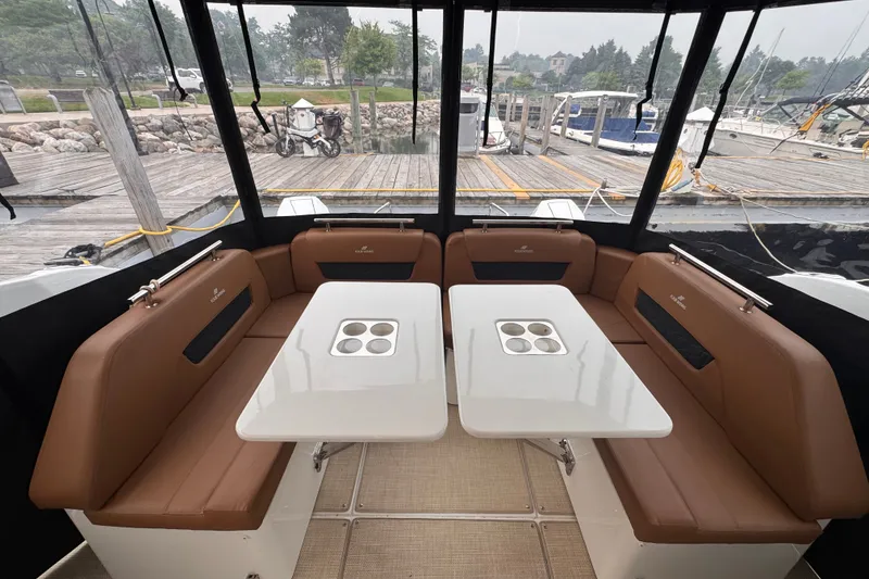Slide: The Image of Interior of 2025 Four Winns TH36 boat with brown seating and white tables at a marina. - 15