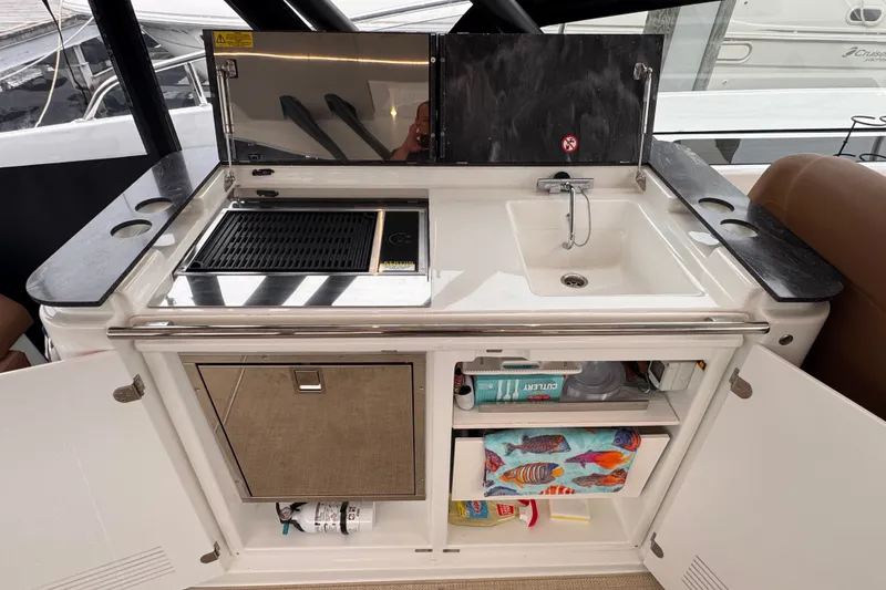 Slide: The Image of 2025 Four Winns TH36 yacht kitchenette with grill, sink, and storage compartments. - 22