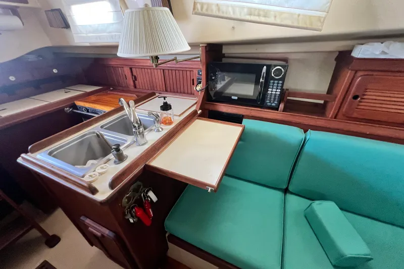 Slide: The Image of Interior of 1987 Island Packet SP Cruiser with kitchenette, sink, microwave, and teal seating. - 61