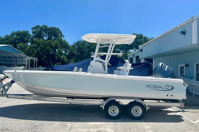 Slide: The Image of 2026 Robalo 246 Cayman boat on trailer, parked outdoors under clear blue sky. - 2