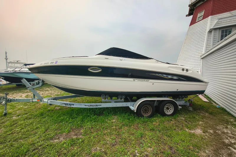 Slide: The Image of 2006 Stingray 250 LR boat on trailer beside a building, parked on grass. - 2
