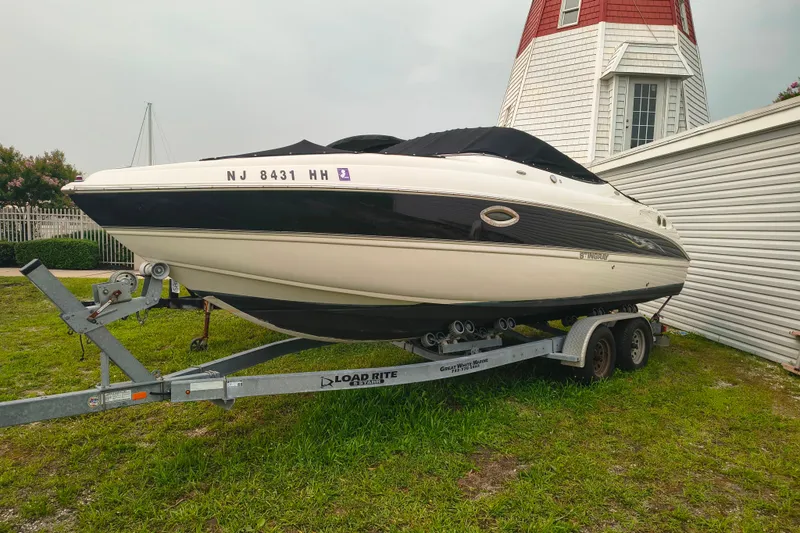 The Image of 2006 Stingray 250 LR boat on trailer near a lighthouse, covered and parked on grass. - 1
