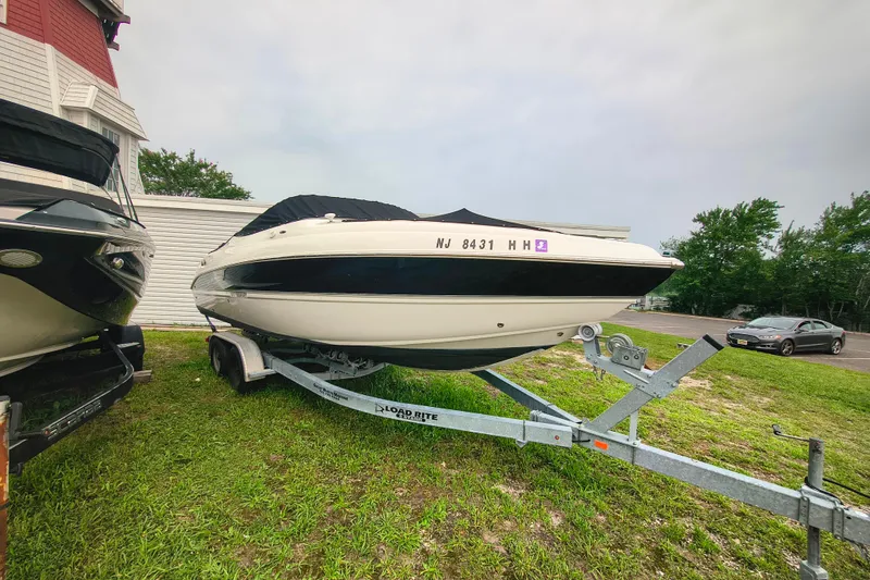 Slide: The Image of 2006 Stingray 250 LR boat on trailer, parked on grass beside a building. - 3