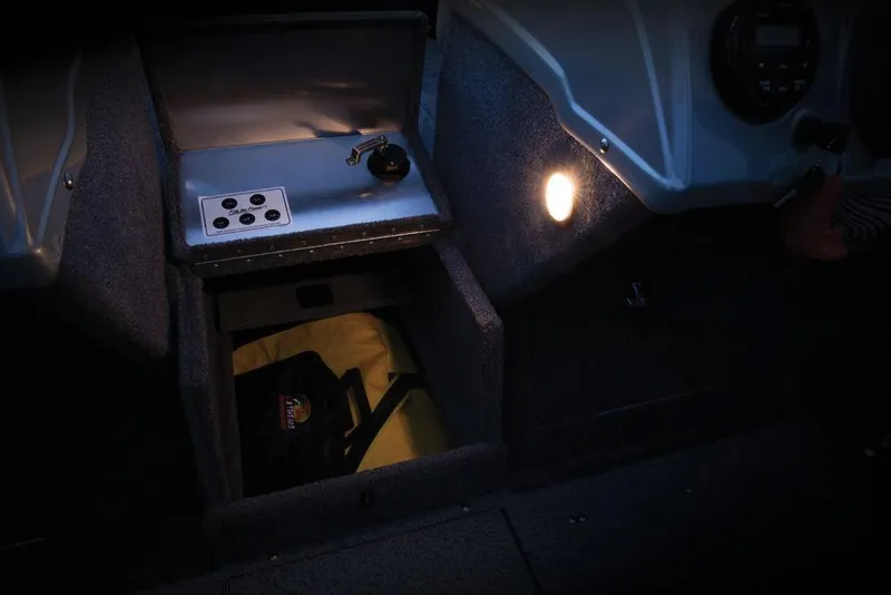 Slide: The Image of The image shows the interior of a 2017 Tracker Targa V-18 WT boat. There's a lit storage compartment with a yellow interior and a control panel with switches. - 47