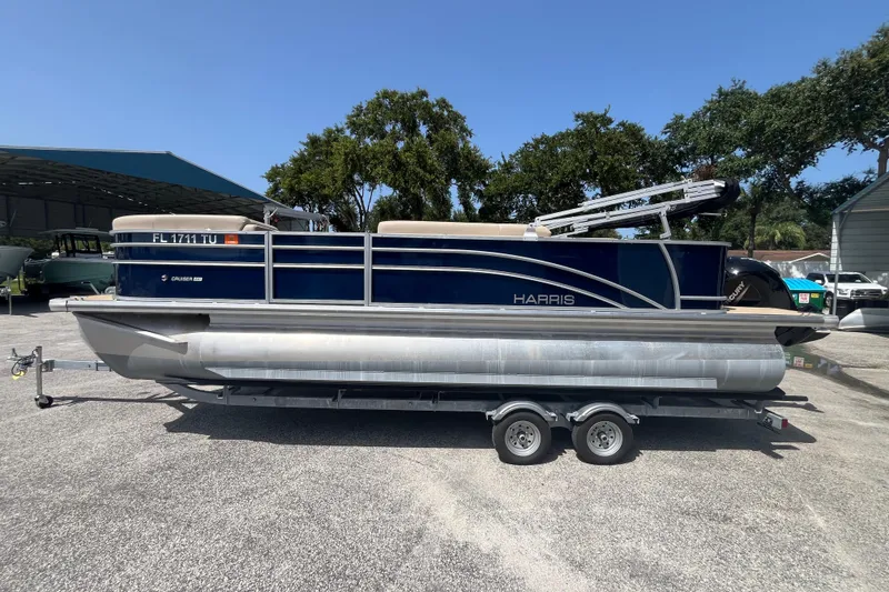 Slide: The Image of 2024 Harris Cruiser 230 pontoon boat on trailer, parked outdoors under clear sky. - 7