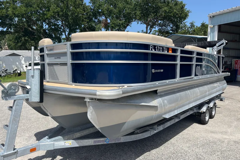 The Image of 2024 Harris Cruiser 230 pontoon boat on trailer, parked outdoors near trees and a building. - 1