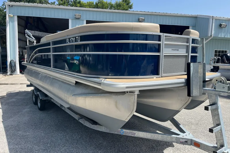Slide: The Image of 2024 Harris Cruiser 230 pontoon boat on trailer outside a metal building. - 3