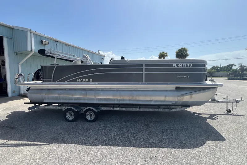 Slide: The Image of 2024 Harris Cruiser 230 pontoon boat on trailer outside a building. - 3