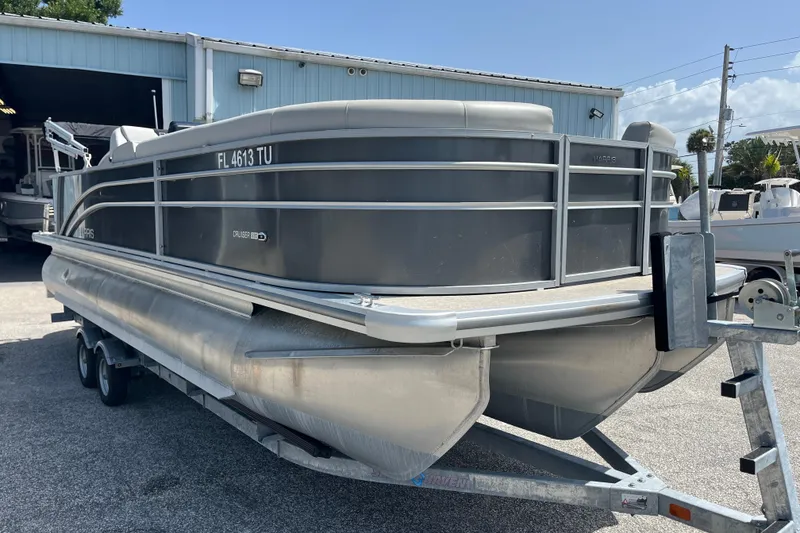 Slide: The Image of 2024 Harris Cruiser 230 pontoon boat on trailer, parked outside a building. - 2