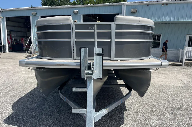 Slide: The Image of 2024 Harris Cruiser 230 pontoon boat on trailer outside a blue building. - 1