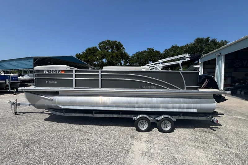 Slide: The Image of 2024 Harris Cruiser 230 pontoon boat on trailer, parked outdoors under clear blue sky. - 7