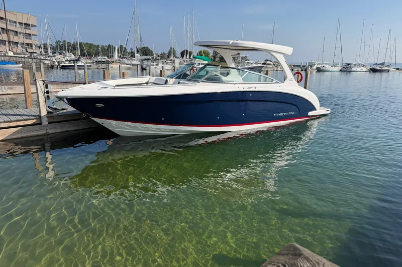 Slide: The Image of 2027 Regal 3300 boat docked in a marina with clear water and sailboats. - 3