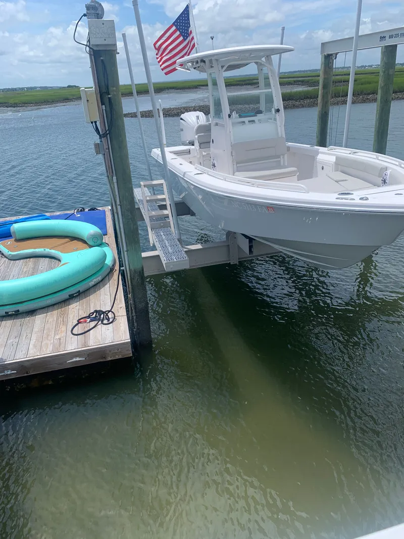 Slide: The Image of A white 2023 Everglades 243 Center Console boat is on a lift at a dock. An American flag waves in the background. - 5