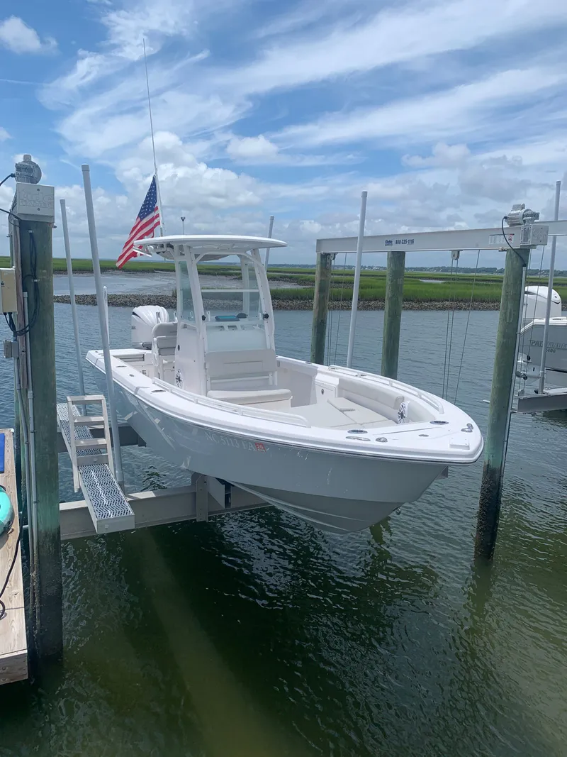 Slide: The Image of A 2023 Everglades 243 Center Console boat is on a lift above the water. It features a white design and an American flag. - 6