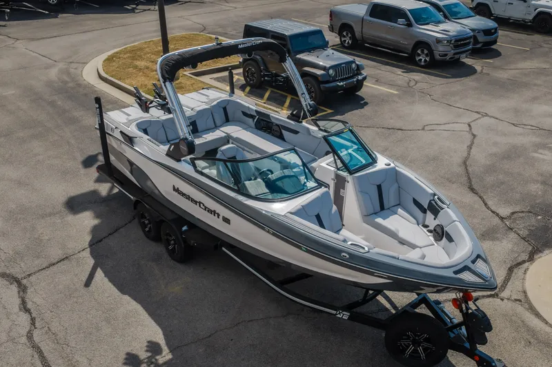Slide: The Image of 2024 MasterCraft XT25 boat on trailer in parking lot, surrounded by vehicles. - 22