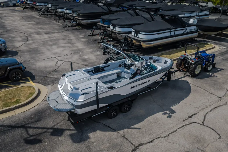 Slide: The Image of 2024 MasterCraft XT25 boat on trailer, parked in a marina lot with covered boats. - 20