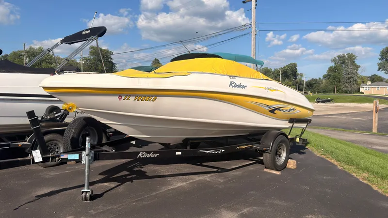 Slide: The Image of A 2002 Rinker 192 Captiva Bowrider on a trailer, with a yellow cover, parked on a lot. - 1