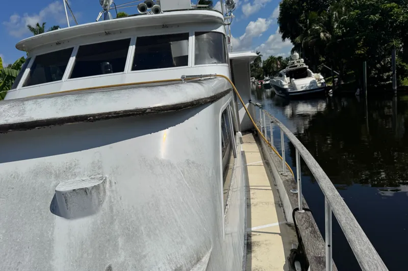Slide: The Image of 1981 Broward 72 Motor Yacht docked on a sunny day, with lush greenery nearby. - 4