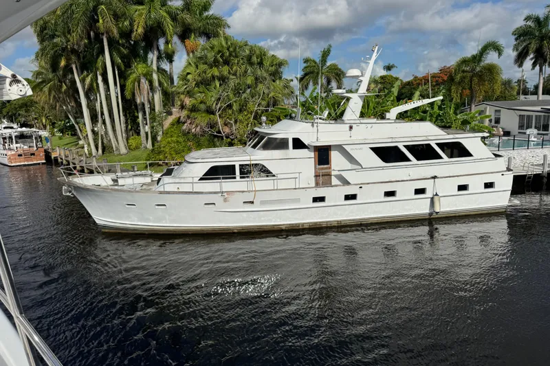 Slide: The Image of 1981 Broward 72 Motor Yacht docked by lush palm trees under a partly cloudy sky. - 1