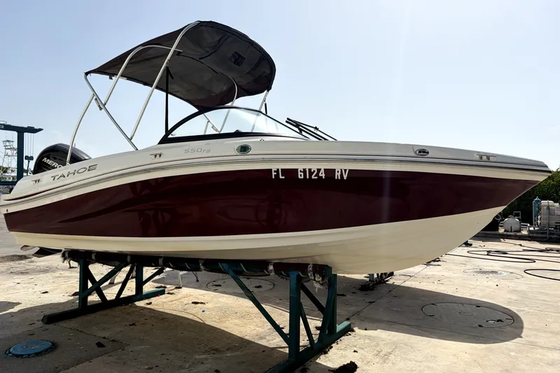 Slide: The Image of 2019 Tahoe 550 TS boat on dry dock, maroon and white exterior, with canopy. - 1
