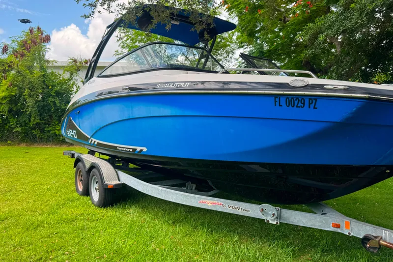 Slide: The Image of 2015 Yamaha Boats AR240 on trailer, vibrant blue hull, parked on grass with lush greenery. - 2