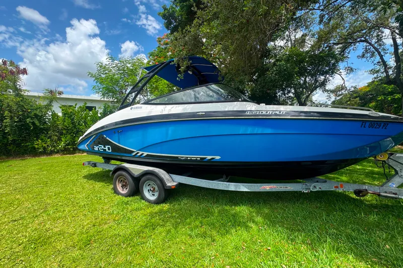 Slide: The Image of 2015 Yamaha Boats AR240 on trailer, blue hull, parked on grass under clear sky. - 1