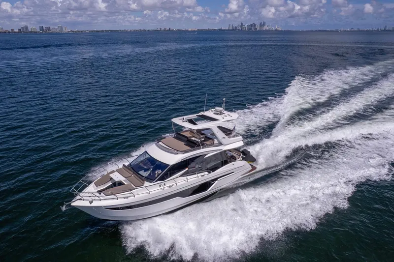 Slide: The Image of 2021 Galeon 500 Fly yacht cruising on open water with city skyline in background. - 8